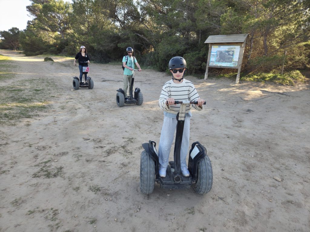 Three people riding Segways on a dirt path in a wooded area.