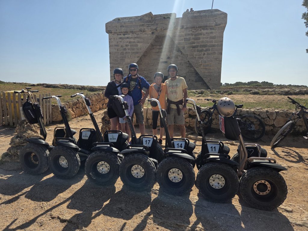 Group of people in helmets standing behind parked segways near an old stone structure.