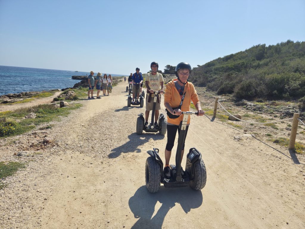 People ride segways on a coastal dirt path under a clear sky.