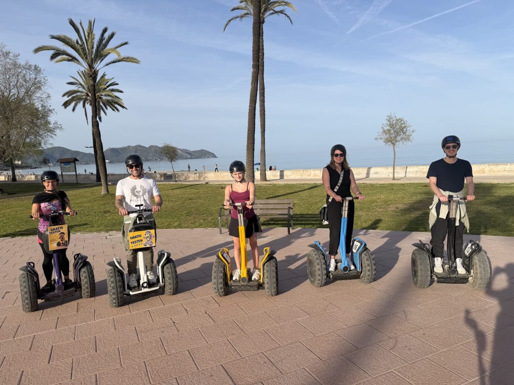 Five people on Segways in a park near a beach with palm trees.