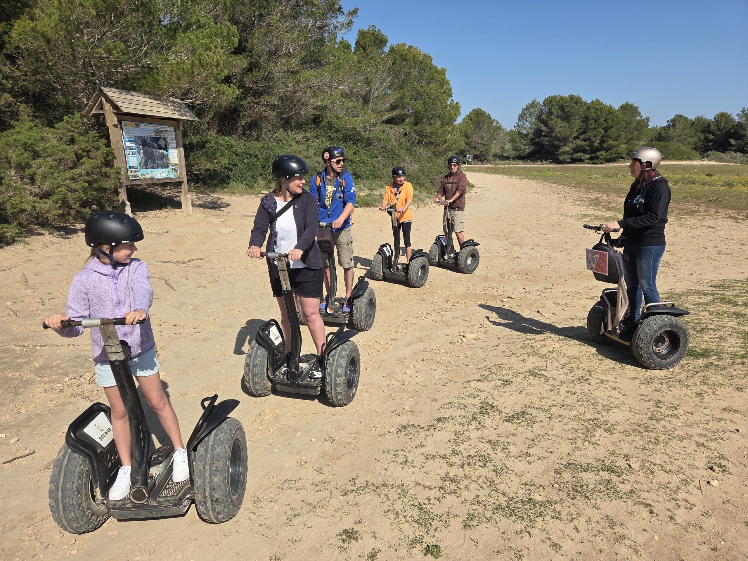Group of people riding Segways on a dirt path near trees.
