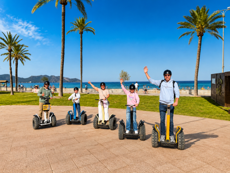 Group of five people on segways near a beach, waving at the camera.